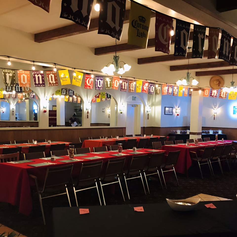 A large dining room at Las Cazuelas Restaurant with red-clothed tables, chairs, and festive Corona banners.