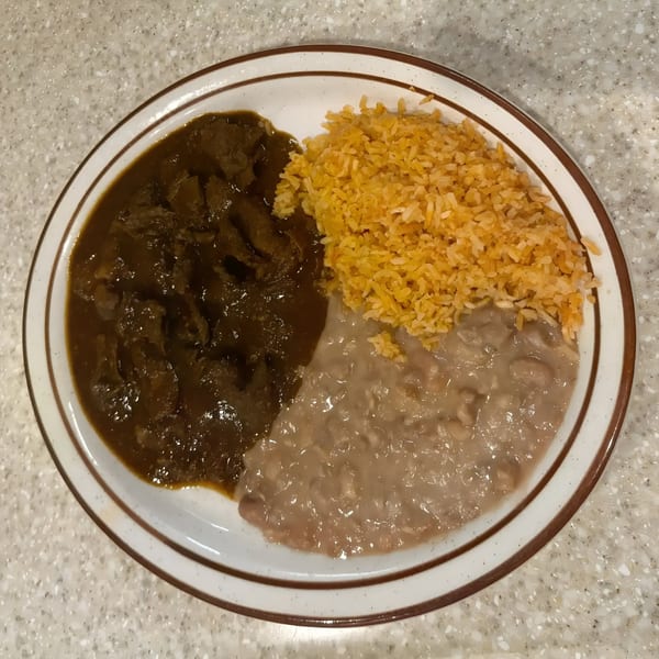 A plate of Mexican food with carne guisada, orange rice, and refried beans on a speckled counter.