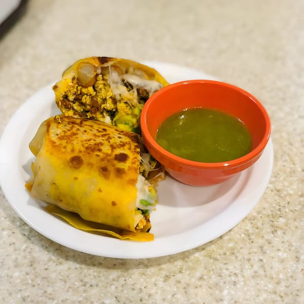 A golden-brown burrito, cut in half to reveal its cheesy filling, served with a side of green salsa.